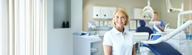 Lächelnde Zahnärztin steht vor einem Zahnarztstuhl.