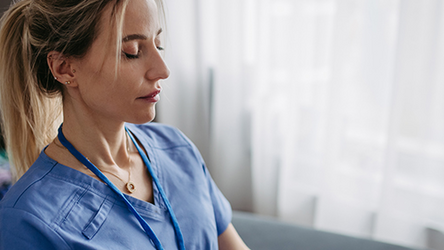 Eine Ärztin sitzt entspannt mit geschlossenen Augen im Schneidersitz und meditiert.