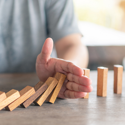 Eine Hand stoppt umfallende Dominosteine.