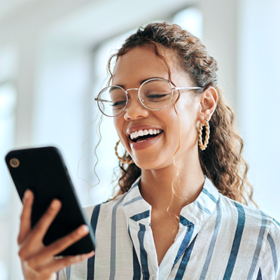 Eine Frau schaut lachend auf ihr Smartphone.