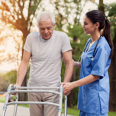 Eine Ärztin begleitet einen Senioren bei einem Spaziergang mit einem Rollator