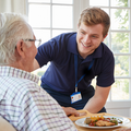 Eine Pflegefachkraft serviert einem Pflegepatienten ein leckeres Mittagessen