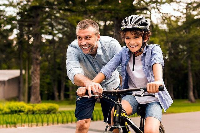 Kind fährt Fahrrad und wird von einem Erwachsenen unterstützt