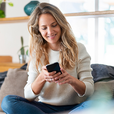 Eine Frau schaut lächelnd auf ihr Smartphone.