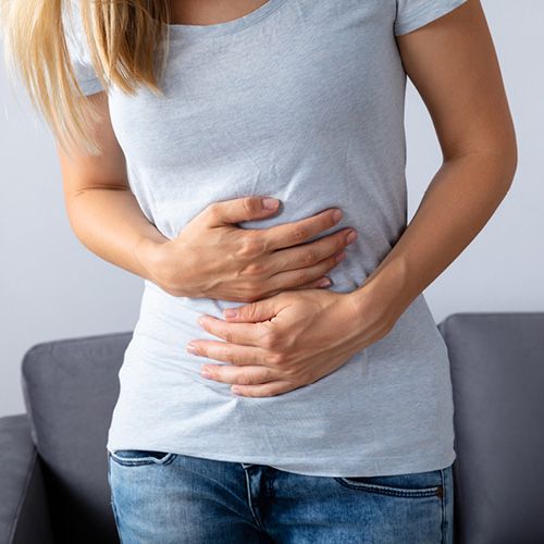 Eine Frau hält ihre Hände auf ihren schmerzenden Bauch.