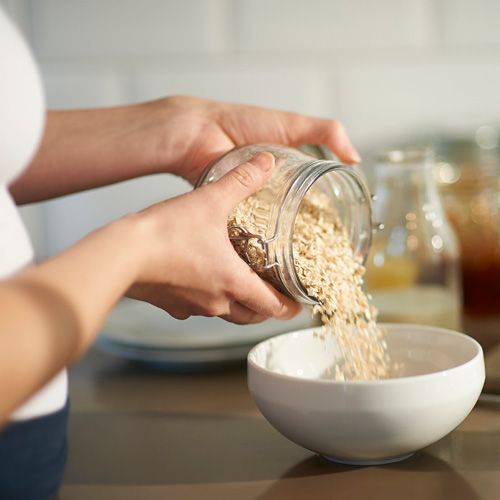 Eine Frau schüttet Haferflocken in eine Müsli-Schale.