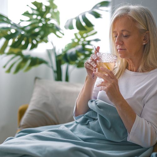 Eine Frau sitzt unter einer Decke mit einer Tasse Tee.