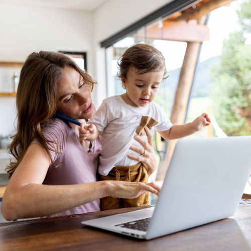 Eine Mutter telefoniert im Home­office und hält ihr Kind auf dem Arm.