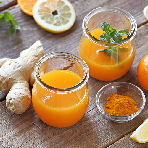 Gepresster Orangensaft mit Ingwer verfeinert steht auf einem mit Ingwer, Ingwerpulver und Orangen dekoriertem Tisch.